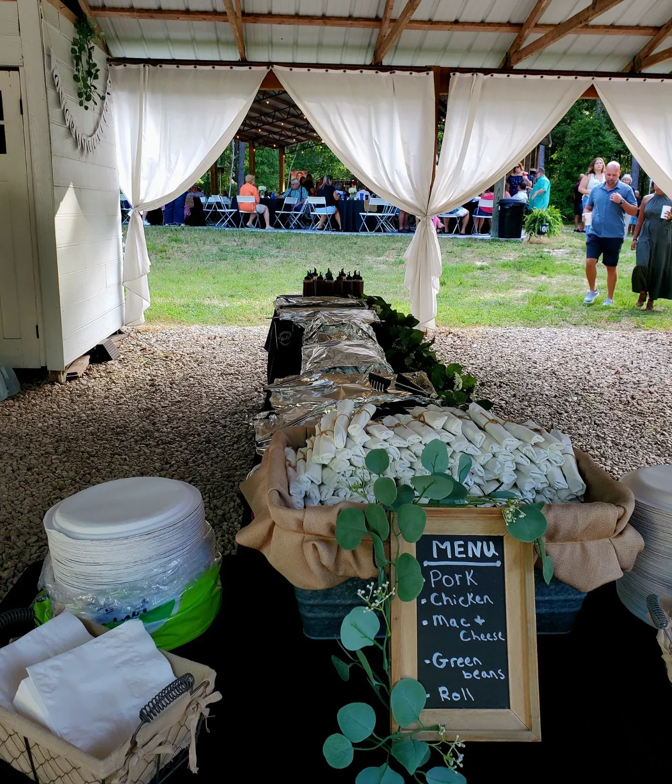 A buffet table with a menu board listing "Pork, Chicken, Mac + Cheese, Green beans, Roll.