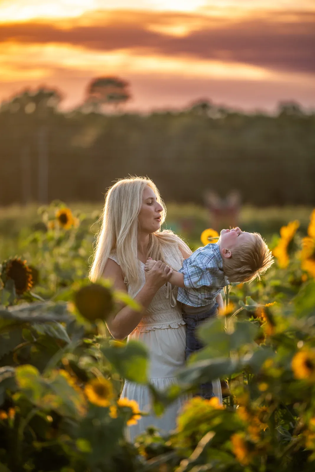 A woman holding a child in a field of sunflowers at sunset.