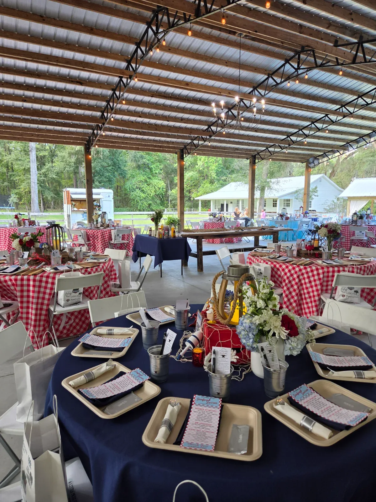 Outdoor pavilion with tables set with red and white checkered and blue tablecloths, and nautical decorations.