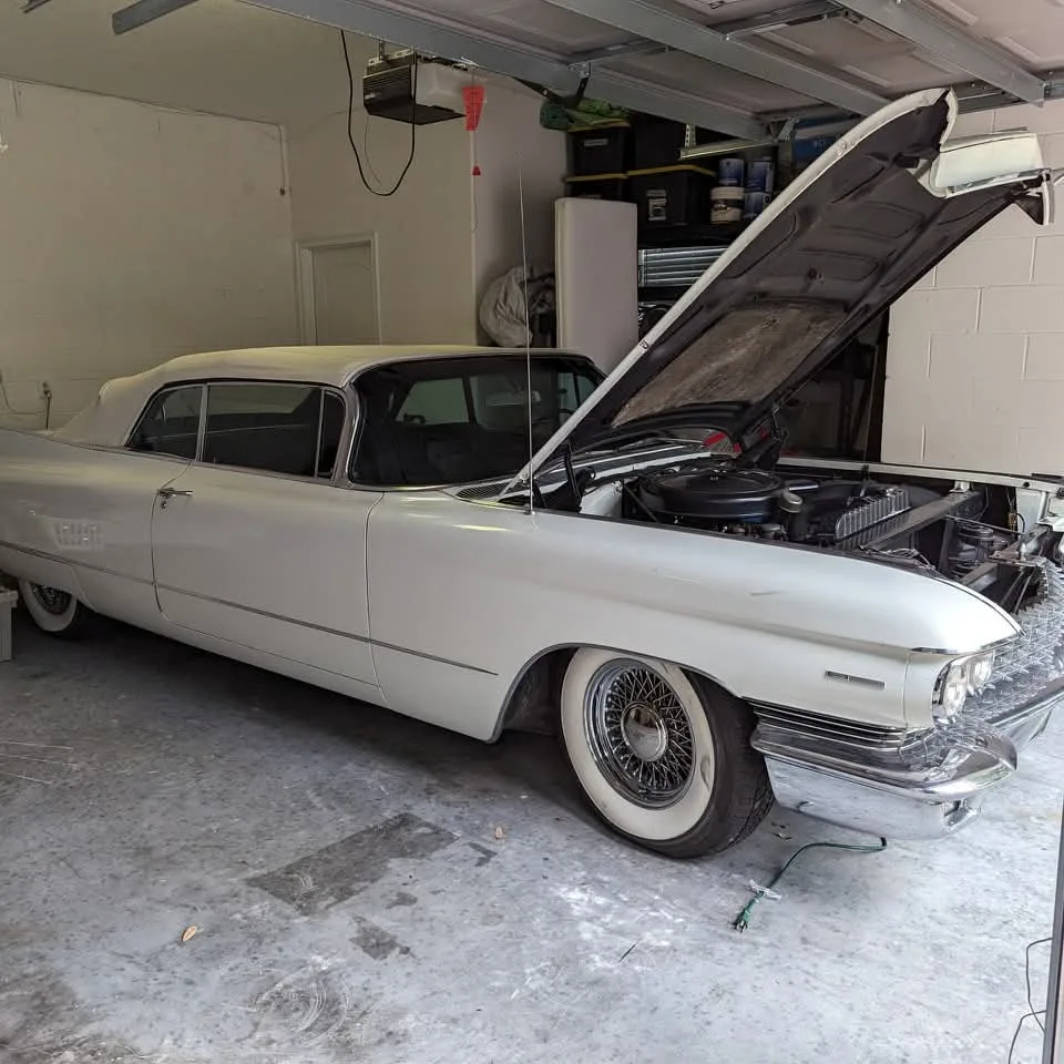 A white vintage car with its hood open, parked in a garage.