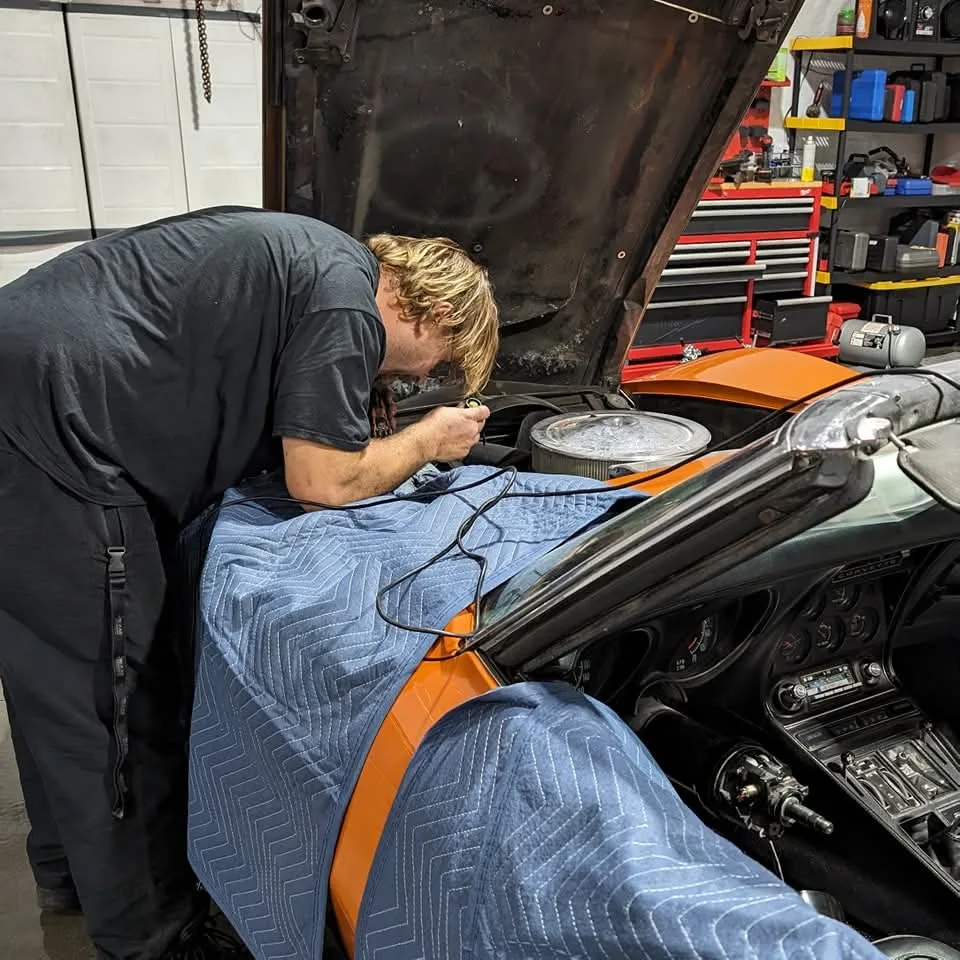 A person in a black shirt works on the engine of an orange car with its hood open.