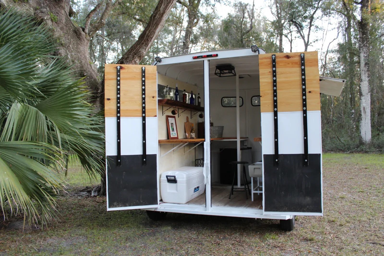 A white trailer with its back doors open, revealing shelves, bottles, and a cooler inside.