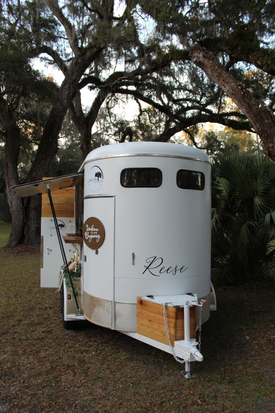 A white trailer with a side hatch open, revealing a wooden counter and a sign that reads "Welcome to our Beginning.