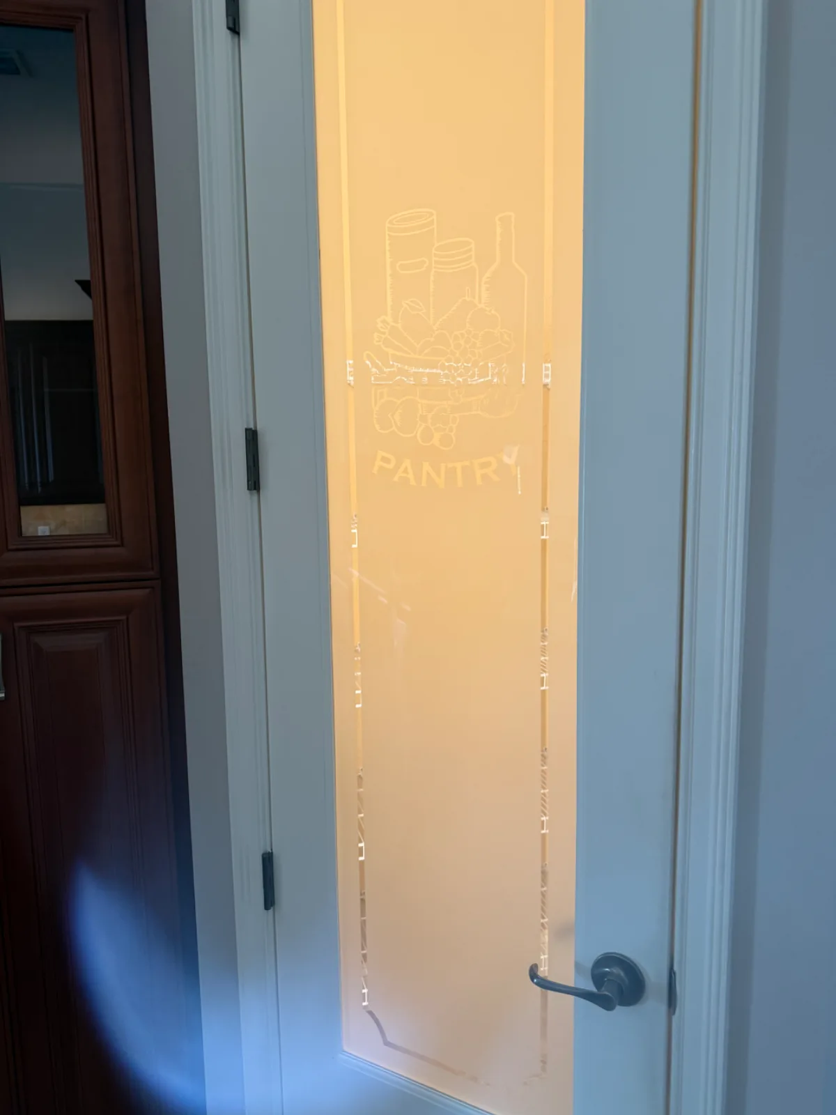 A white door with a frosted glass panel etched with food items and the word "PANTRY.
