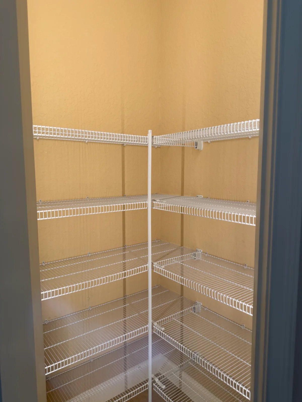 An empty pantry with light orange walls and white wire shelving.