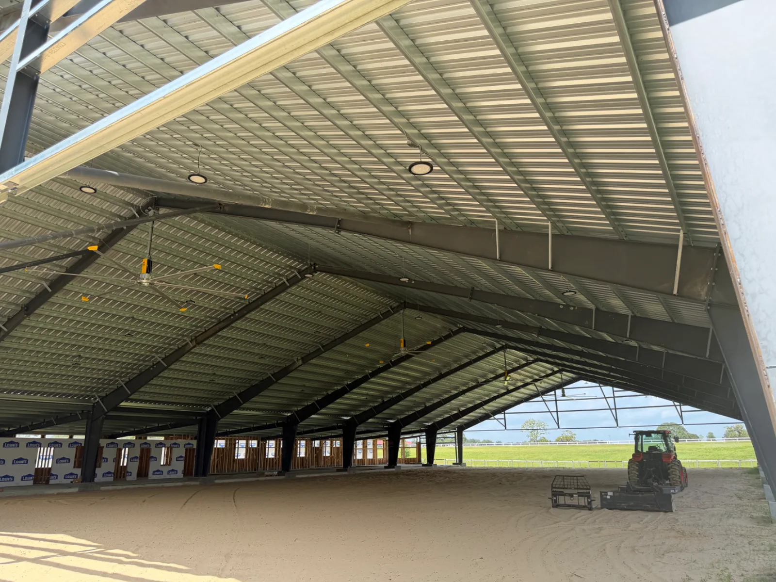 Interior of a large metal building with a dirt floor, open sides, and a red tractor.