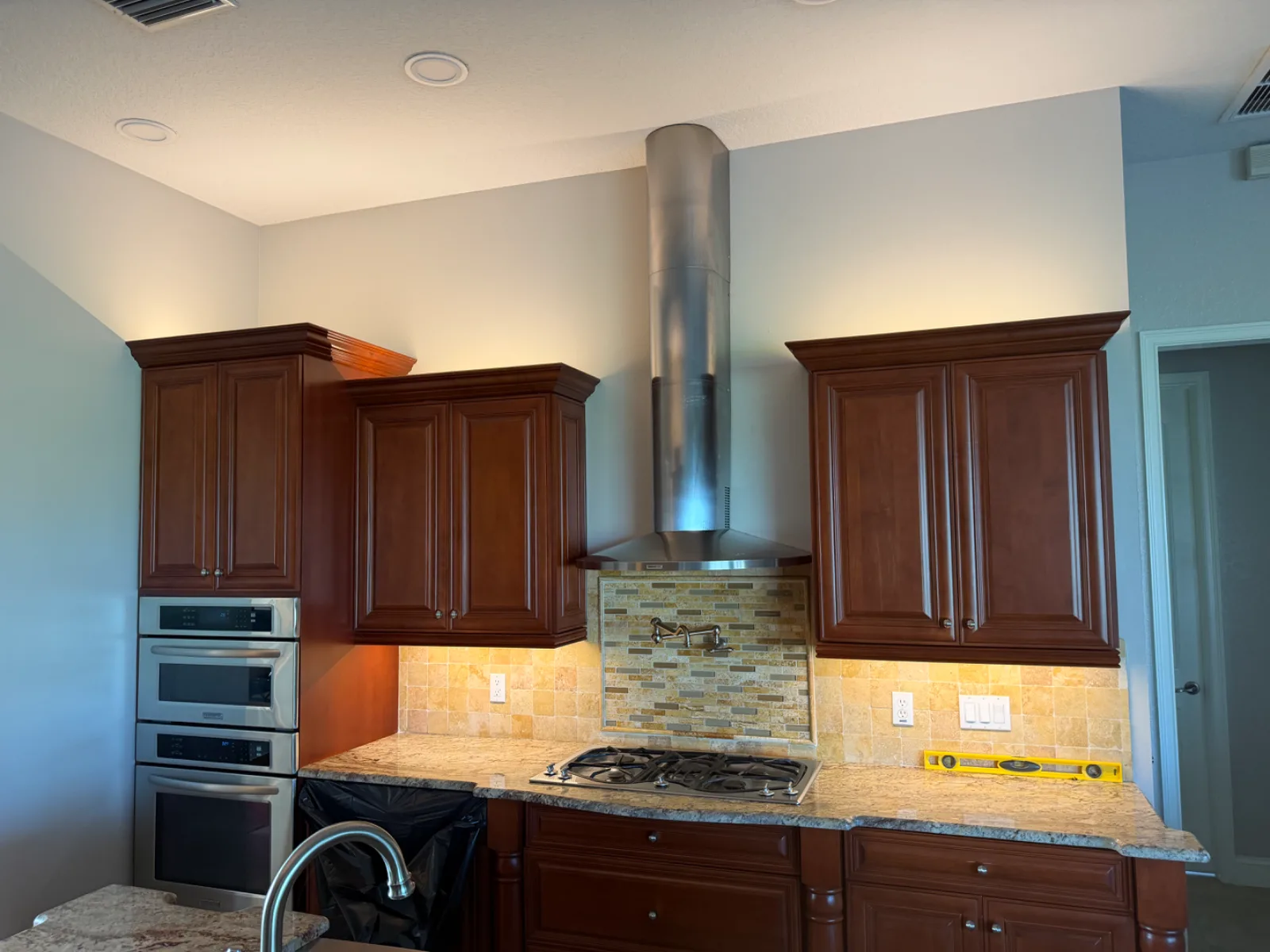 A kitchen with brown cabinets, stainless steel appliances, a tiled backsplash, and granite countertops.