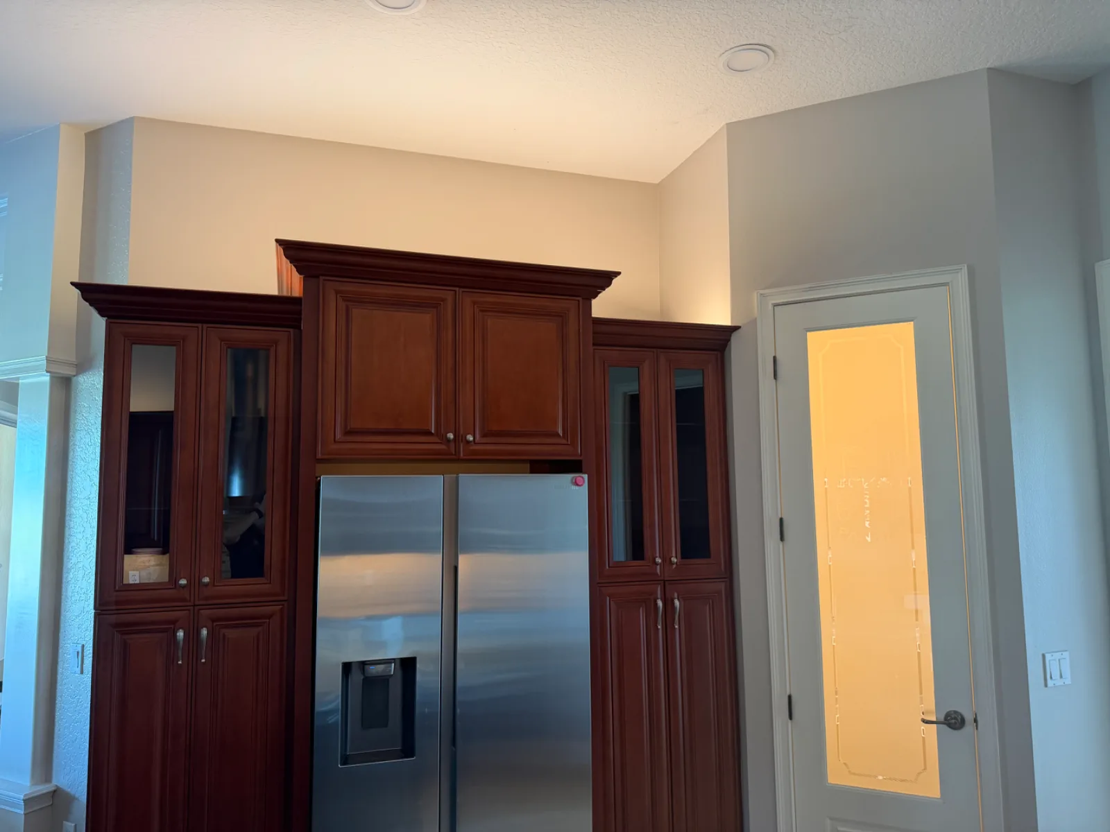 A stainless steel refrigerator is surrounded by dark wood cabinets next to a white door with a frosted glass panel.