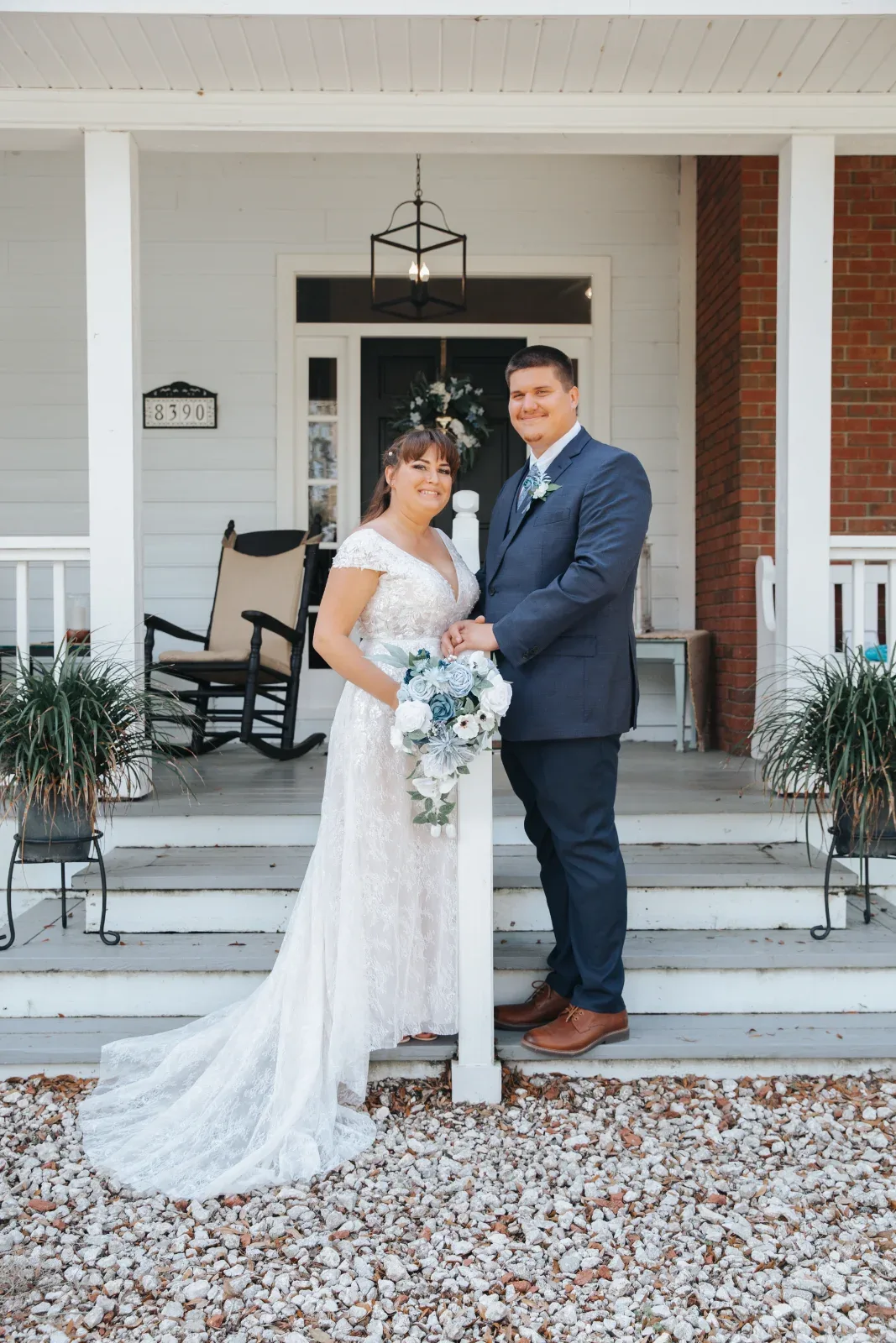 A couple stands on a white porch with a house number 8390 visible.