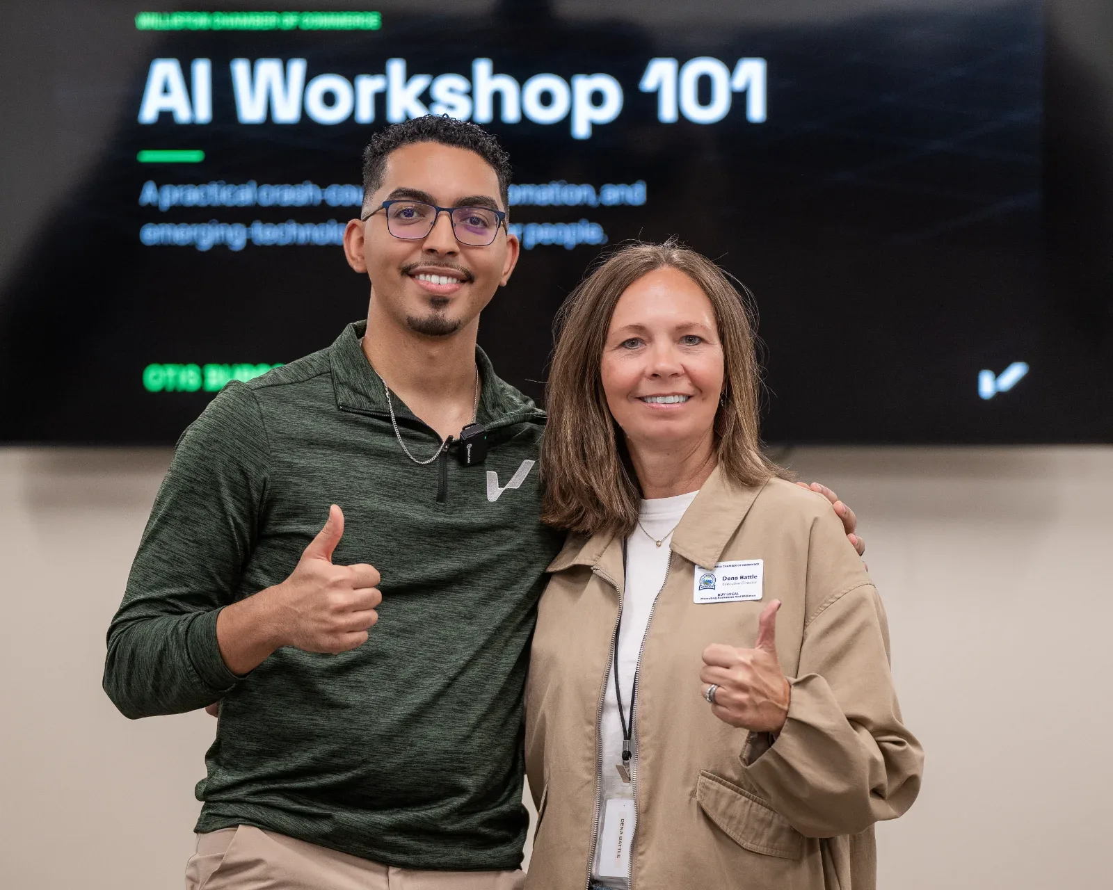 Two people smiling and giving thumbs up in front of a screen displaying "AI Workshop 101".