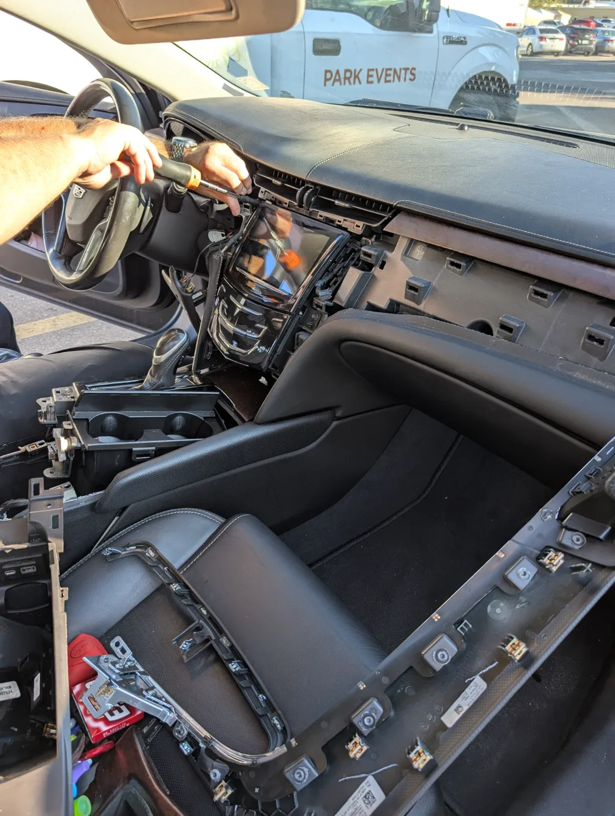 A person uses a screwdriver to work on the dashboard of a car with interior panels removed.